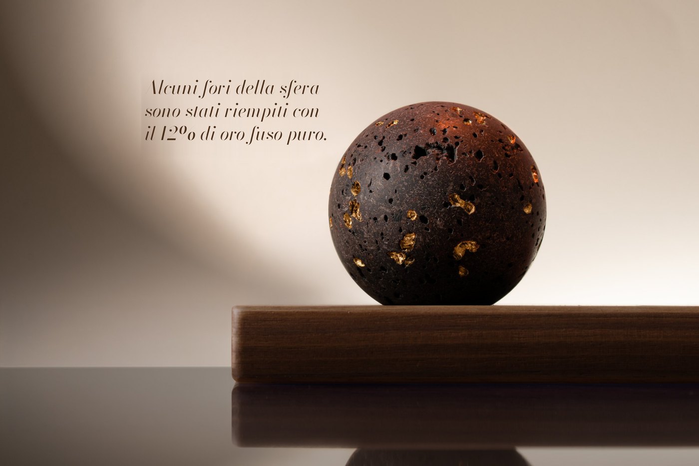 La sfera di lava sulla base in noce. Testo nell'immagine: «Alcuni fori della sfera sono stati riempiti con il 12% di oro fuso puro.»